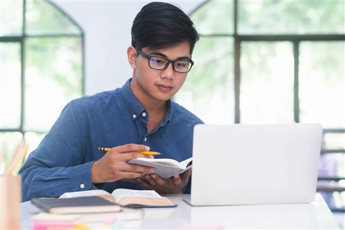 Teenage student with notebook and pencil sitting in front of laptop